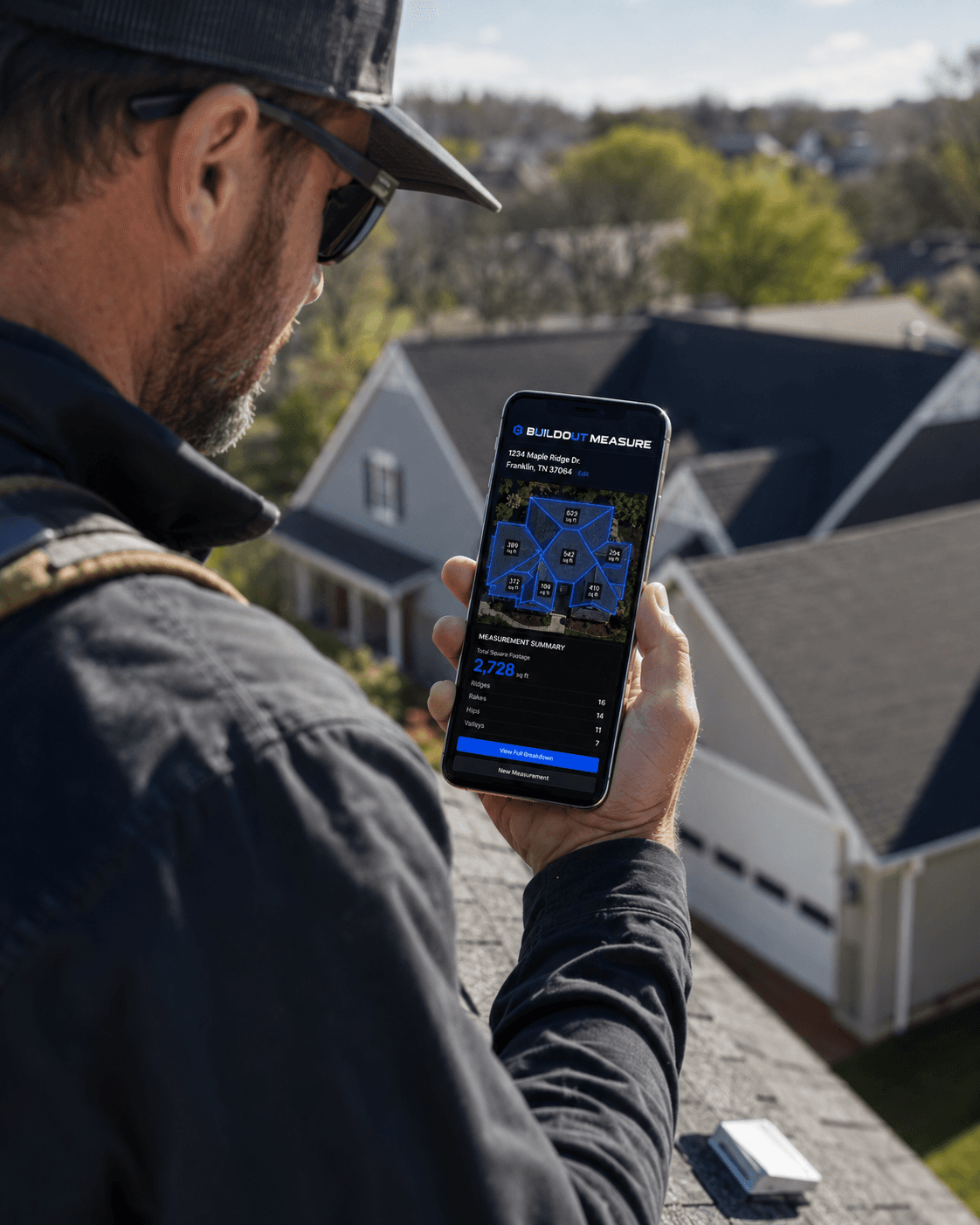 Roofer on a roof holding a phone with the Buildout Measure app open — running a measurement report from the jobsite